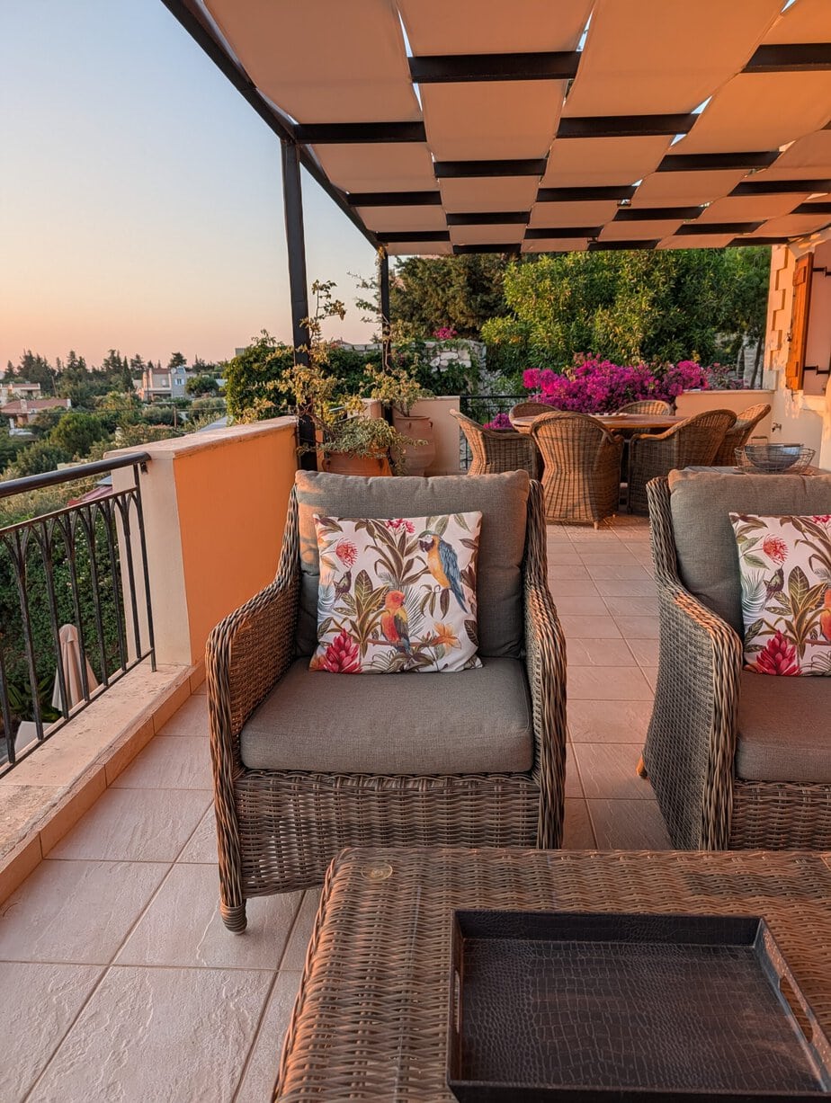 Lounge chairs and dining table on the Villa Koumos veranda in warm evening light