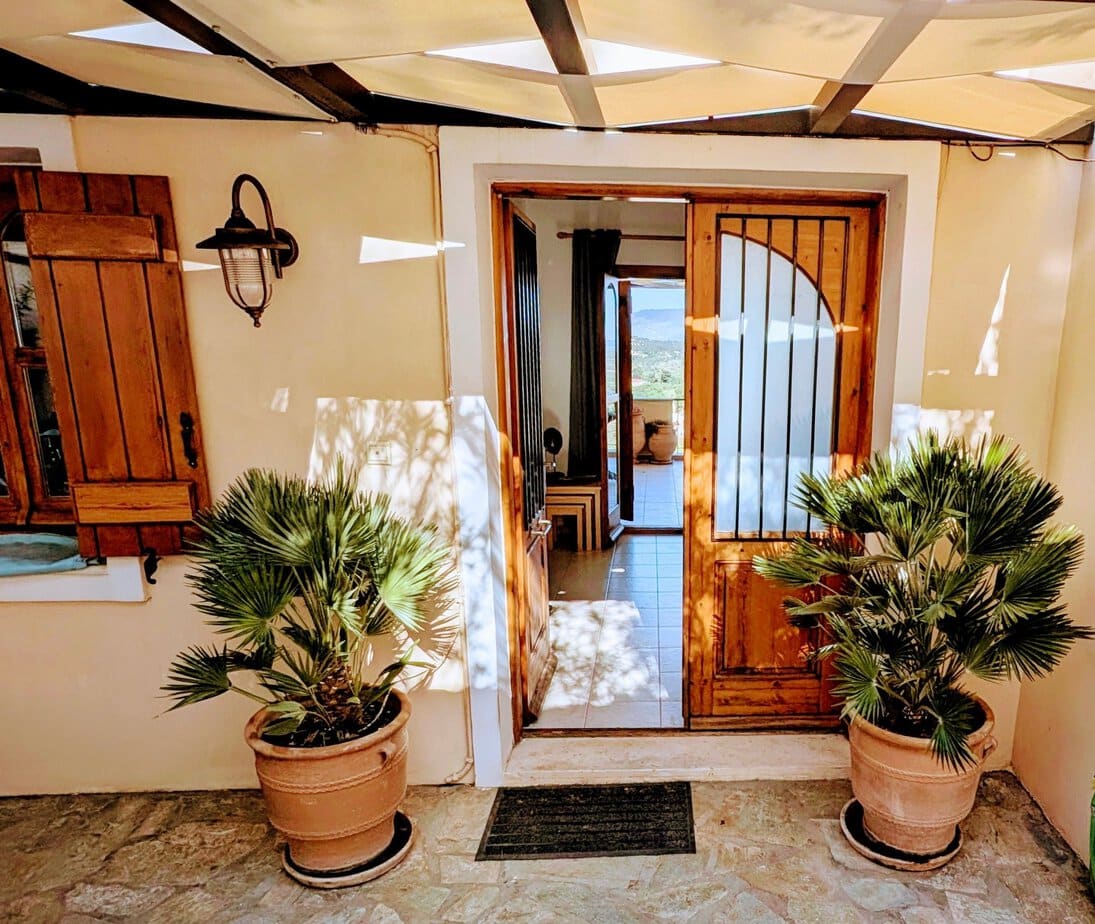 Front entrance to Villa Koumos in Gavalochori with timber doors, whitewashed walls and potted palms