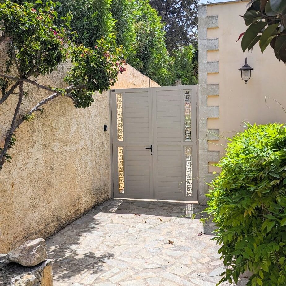 Closed gate leading to the courtyard of Villa Koumos, framed by stone walls and lush greenery, inviting guests into this wonderful luxurious holiday villa in Crete